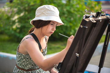 Cute teenage girl drawing at easel outdoors, diy