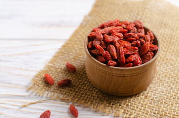 Dried goji berries in a wooden bowl on a burlap cloth on a white wooden table. Superfood. Vegetarian, vegan. Healthy food concept. Horizontal orientation