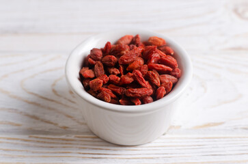 Dried goji berries in a white bowl on a white wooden table. Superfood. Vegetarian, vegan. Healthy food concept.