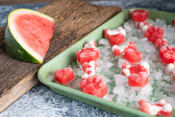 Frozen, watermelon dog treats on ice in a green sheet pan.