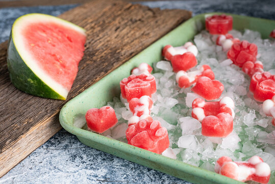 Frozen, watermelon dog treats on ice in a green sheet pan.