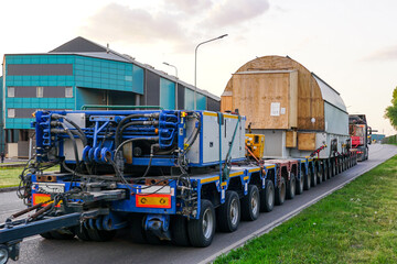 Very long specialized multi axle truck trailer carries very heavy oversize load, rear view