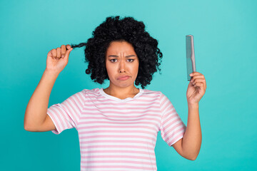 Photo of young beautiful lady in striped t shirt upset holding to untangle her hair using comb isolated on aquamarine color background