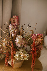 Dry hydrangea, poppy and amaranth in stylish vase close up. Fall decor in modern living room. Thanksgiving and Halloween. Autumn floral arrangement