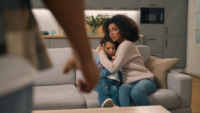 Domestic violence African American ethnic family. Aggressive man father threaten beat clenched fist back view scared mother protect frightened little boy child kid suffering physical abuse indoor home