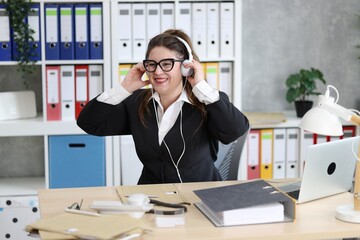 Sekretärin mit Brille, in Bluse und Sakko, hört lachend Musik mit Kopfhörern, Hände am...