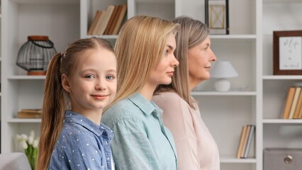 Cute little girl posing indoors with young mother and senior grandmother, side profile view,...