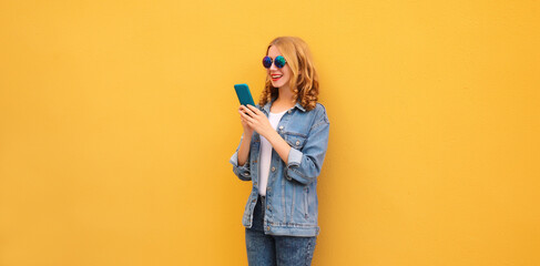 Happy young woman with phone, modern smiling girl looking at smartphone in casual denim clothing