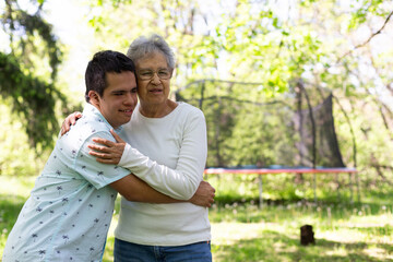 A man and an old woman embrace in a park. The man is wearing a blue shirt . The scene is peaceful and touching.