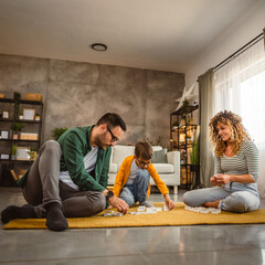 Dad, mum and son play dominoes together on the floor at living room © Miljan Živković