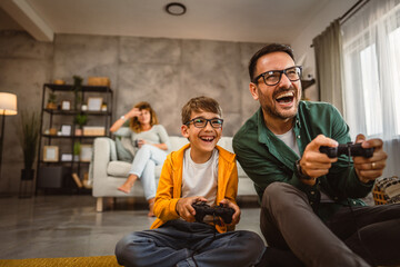 Dad and son play video games with joystick while mum wife watch them