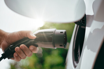 Electric car or ev is charging at station . man use the white power cable and plug on nature background