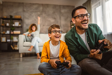Dad and son play video games with joystick while mum wife watch them © Miljan Živković