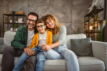 Portrait of mother and father with son sit on sofa in the living room