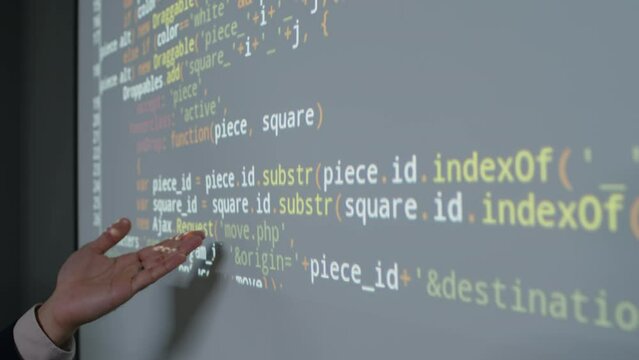 Close-up shot of hand of unrecognizable male teacher pointing to lines of computer code in programming language on projector screen and explaining principles of algorithm development
