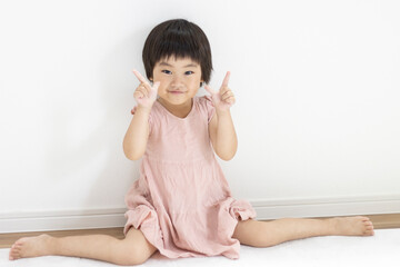 Fototapeta premium 女の子座りでピースする笑顔の女の子（3歳、日本人、ショートヘア）