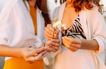 The sparklers in the hands of young women on the beach. Happy women walking with sparkler fireworks on beach. Summer holidays, party, vacation, relax and lifestyle concept.