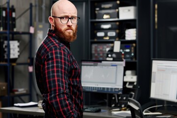 A finance trade manager with a serious expression analyzes stock market indicators on multiple computer screens in a modern office setting.