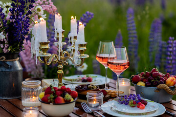 Beautiful romantic outdoor wedding decor in a field. Table decorated with purple lupines flowers. Wineglasses with white wine. Sunset, summer, golden hour. Perfect surprise date for loving couple
