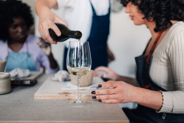 Close up of hand pouring wine in wineglass while artisans doing claywork