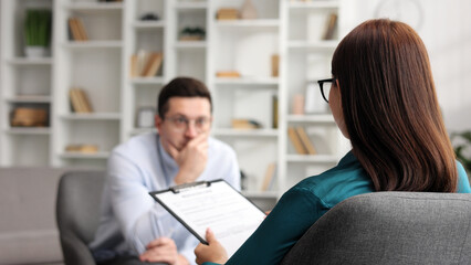 Female psychologist listening to her depressed male patient and taking notes, mental health and counseling concept.