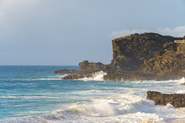 A blurry image of a beach with waves crashing on rocks under the sky