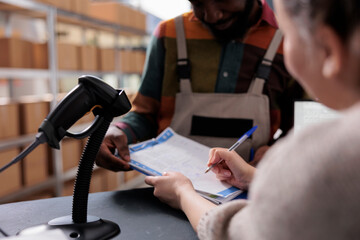 Diverse team analyzing merchandise checklist signing report in warehouse, discussing products quality control. African american employee wearing industrial overall, working at clients orders. Close up