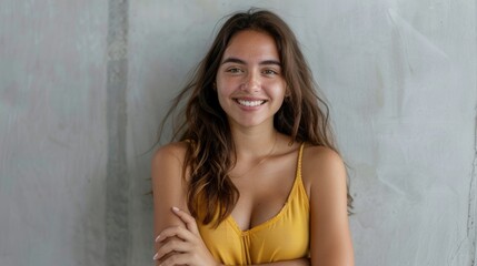 Naklejka premium A young Hispanic woman with long brown hair smiles warmly at the camera. She stands with crossed arms against a grey wall. Generative AI