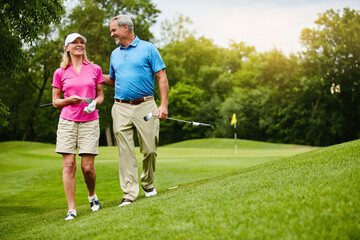 Obraz premium Mature, couple and walking for golf in nature, outside and healthy fitness activity with golfers together with club. Relaxing, weekend break and happy with smile or sport, outdoor exercise and people