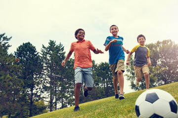 Obraz premium Soccer ball, running and boy children in park for bonding, games and outdoor holiday together. Sports, kids and happy friends playing on grass with smile, fun and energy on summer camp for football.