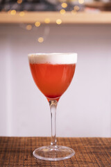Red cocktail with whipped cream in glass on wooden table with bokeh