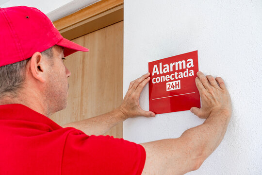Technician installing an alarm sign in spanish "alarm connected 24 hours". Home security installation.