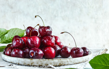 Ripe cherries, cherries in a ceramic plate surrounded by leaves on a light background close-up. A healthy summer dessert.