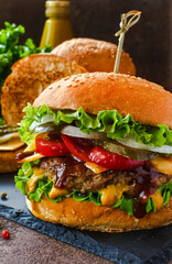 Burger with beef, mustard, sauce, cheese and vegetables on a black plate. Dark background. Delicious burger, street food, fast food.