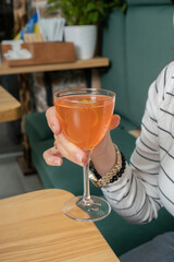 Alcoholic cocktail in woman hand over wooden cafeteria table