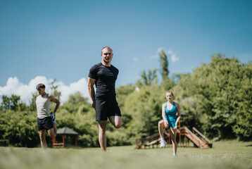Fototapeta premium Three people performing outdoor exercises in a park under a clear blue sky. They are participating in a group workout session.