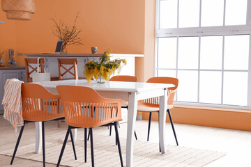Stylish interior of light kitchen with mimosa flowers on dining table