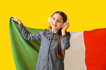 Little girl with flag of Italy listening to music on yellow background