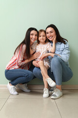 Young lesbian couple with adopted little girl hugging near green wall