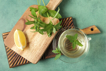 Wooden boards with cup of fresh mint tea with lemon on green background