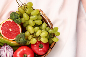 Wicker basket with different fresh fruits and vegetables on table