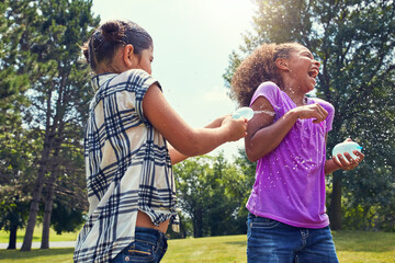 Kids, playing and water balloon for friends in a park with splash fun, sun and bonding in nature....