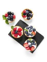 Board of tasty tartlets with whipped cream and berries on white background