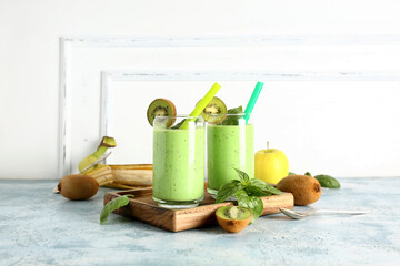 Glasses of fresh kiwi smoothie with basil on blue table