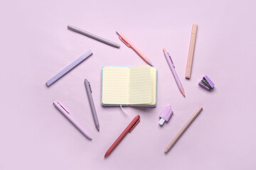 Notebook with different stationery supplies on lilac background
