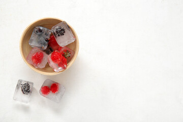 Bowl with frozen berries in ice cubes on white background