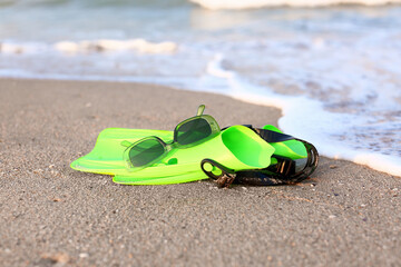 Stylish sunglasses with flippers on sand