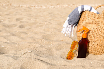 Obraz premium Straw bag with bottle of sunscreen cream, blanket and sunglasses on sandy background