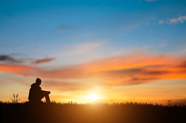 Silhouette of young man sits and praying alone at the top of the mountain at sunset with beautiful natural sunlight.