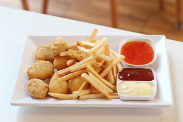 Snack platter (nuggets and sauce) on white plate on wooden table.